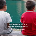 Zwei Jungen sitzen am Seeufer auf einer Bank. Text im Bild: ‚Im Schatten der Sucht – Über die leisen Gefühle der Geschwisterkinder‘.