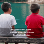 Zwei Jungen sitzen am Seeufer auf einer Bank. Text im Bild: ‚Im Schatten der Sucht – Über die leisen Gefühle der Geschwisterkinder‘.