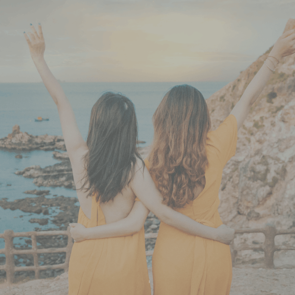 Zwei Frauen stehen umarmt am Meer und schauen gemeinsam in die Ferne